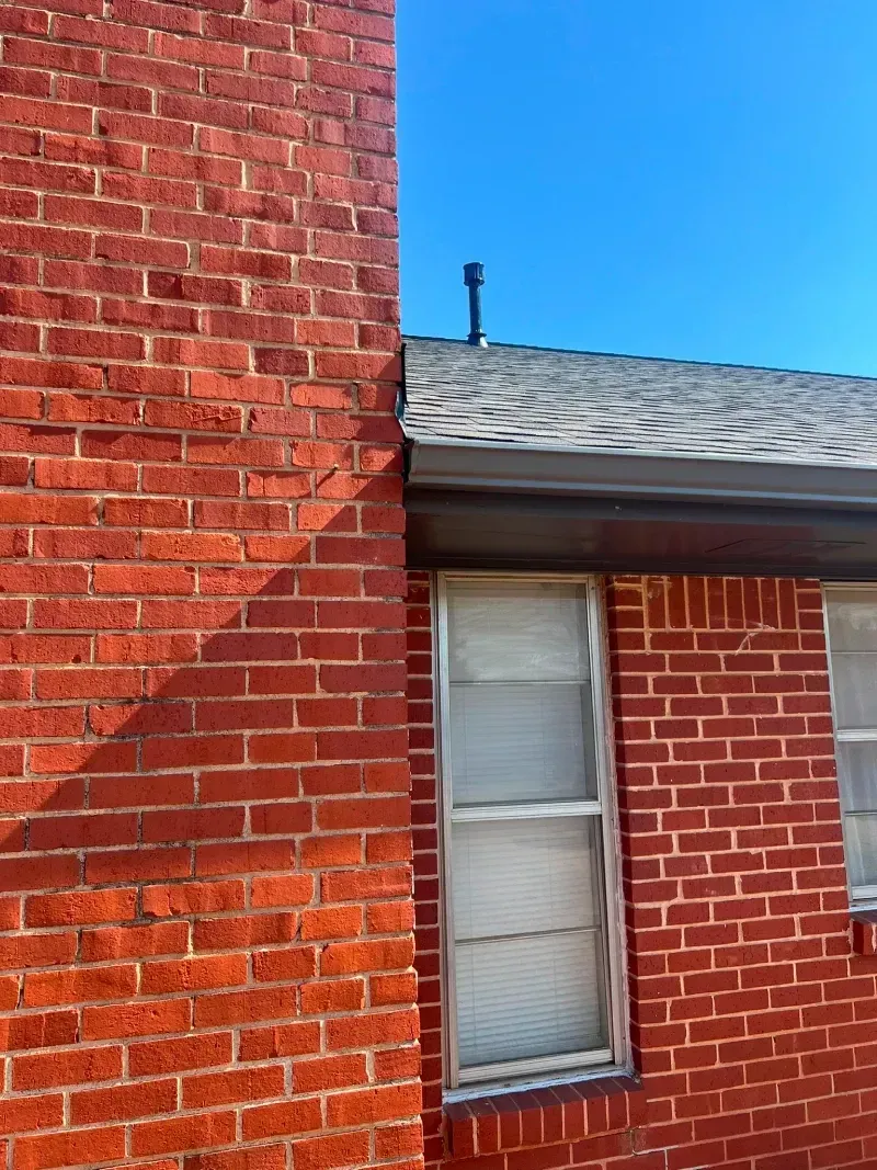 Red brick chimney next to a building with gray shingles and a window.