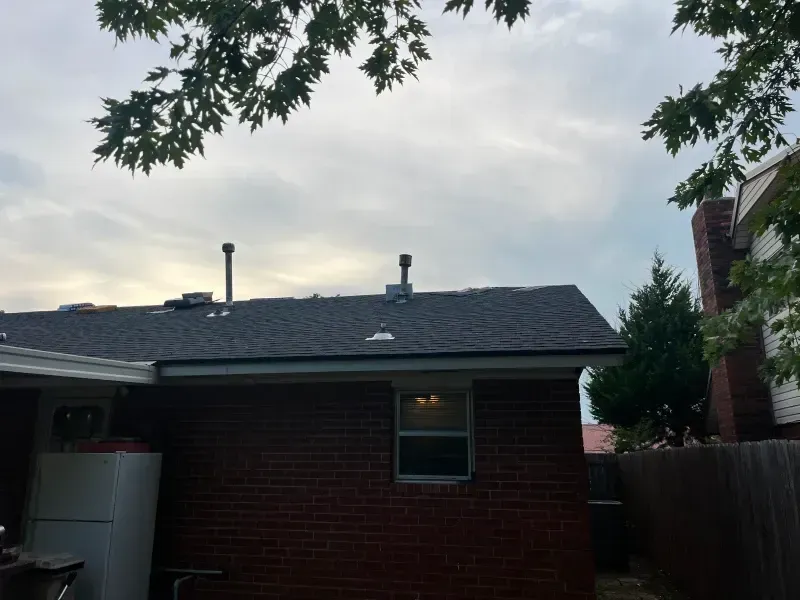 Brick house exterior with a dark roof and two metal chimneys against a cloudy sky.