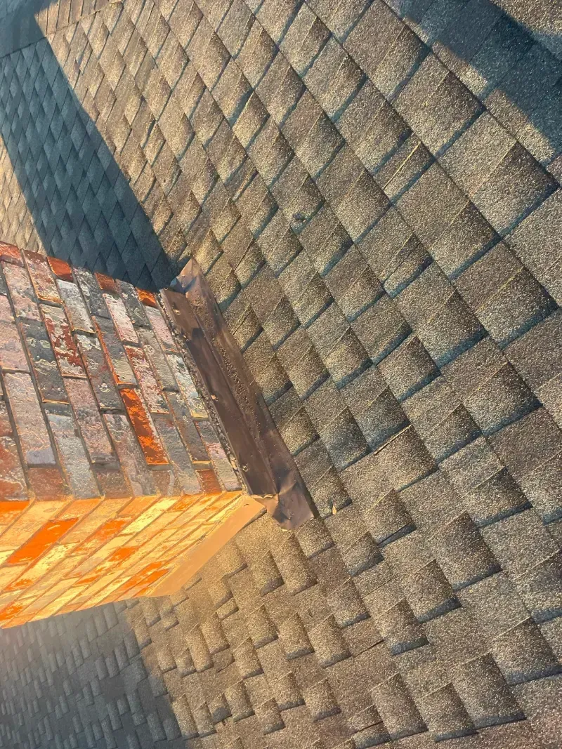 Close-up of a brown shingled roof with a red brick chimney.