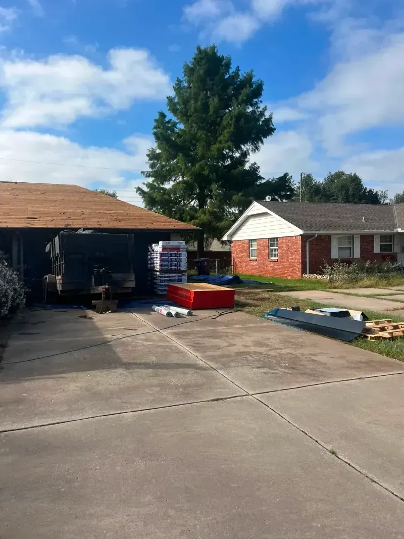 A home with roofing materials in the driveway, blue sky.