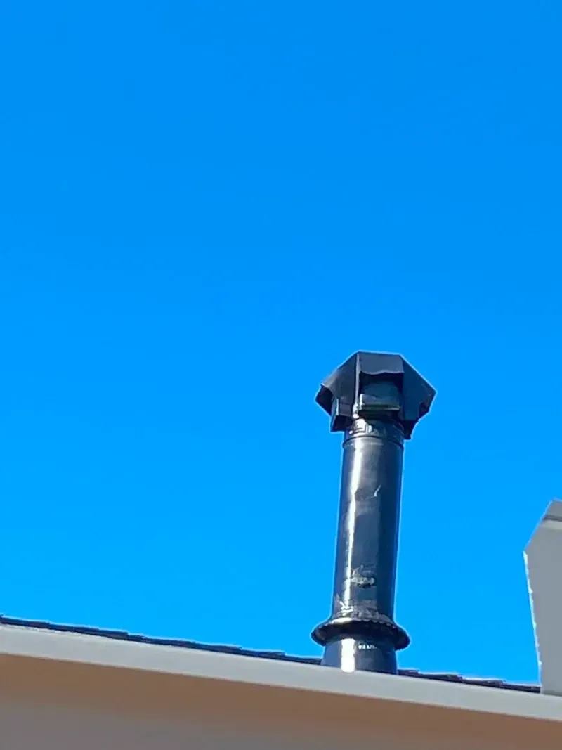 Black chimney on a rooftop against a clear, blue sky.