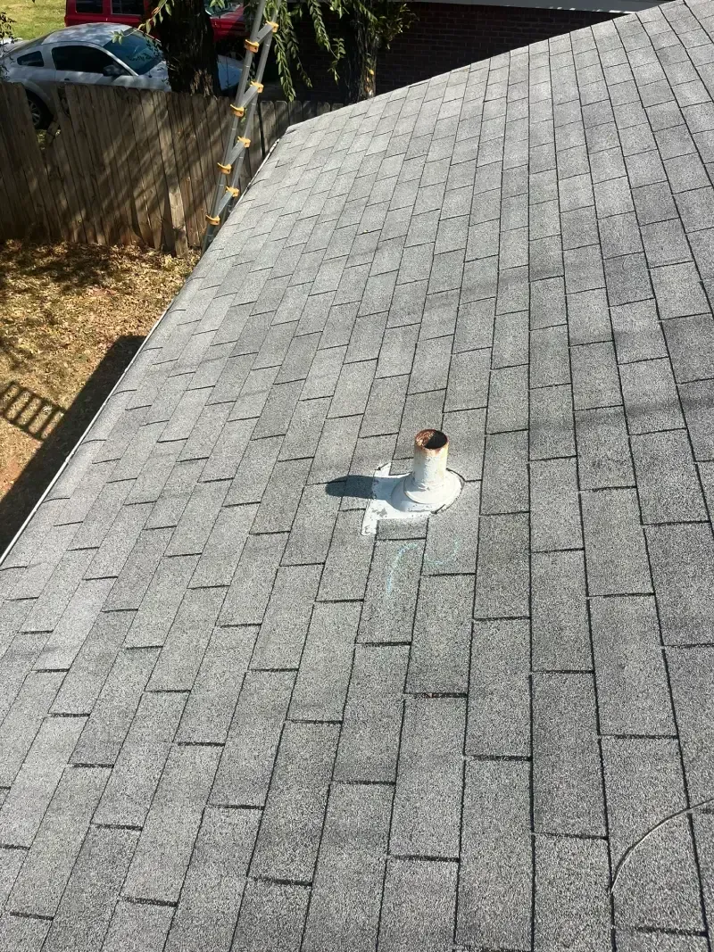 Gray shingled roof with a vent pipe and sunlight casting shadows.