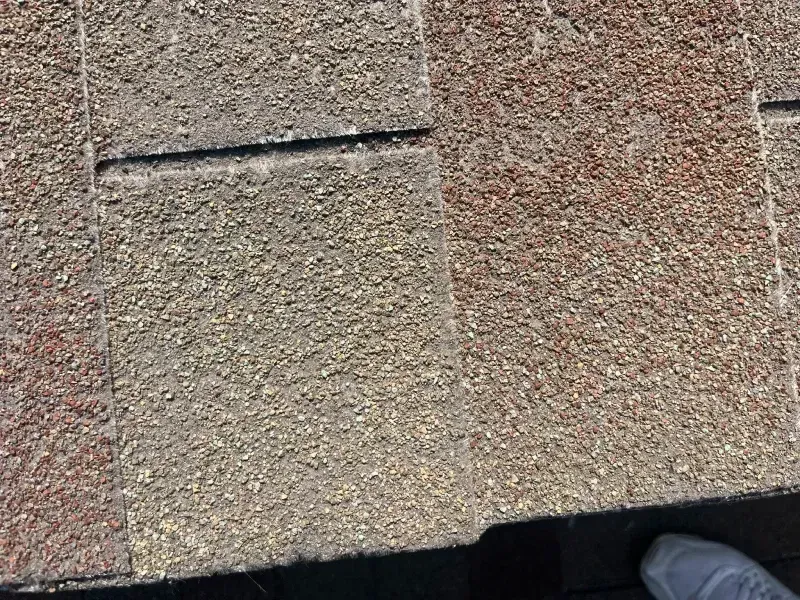 Close-up view of weathered asphalt roof shingles, showing granular texture in shades of brown and gray.