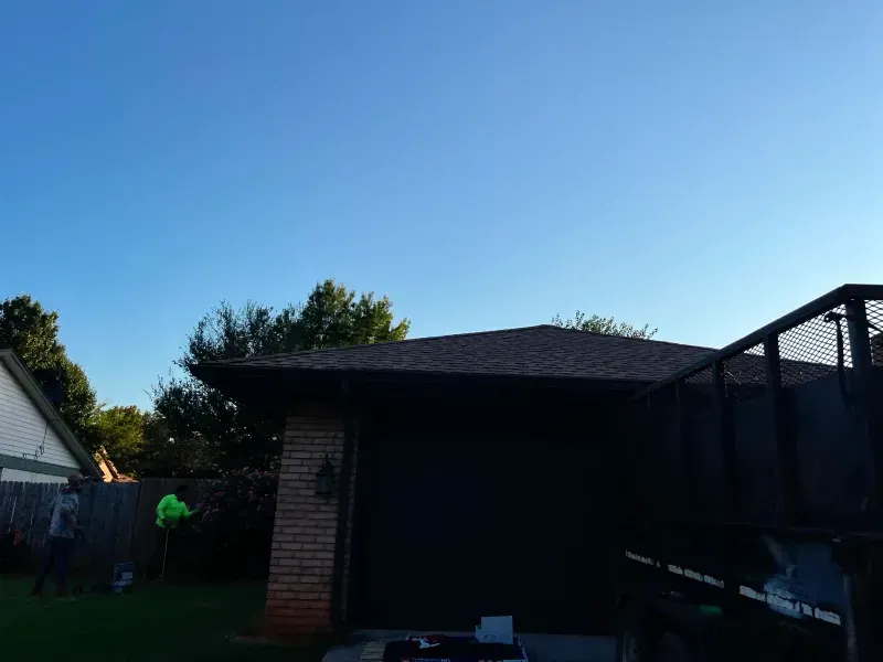 A dark-roofed building with a brick wall, part of a trailer, and blue sky.