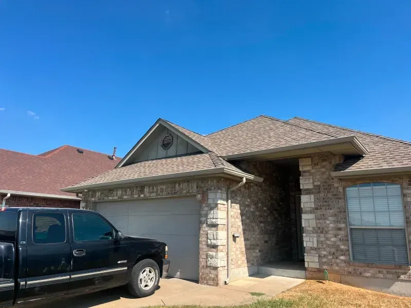 A one-story brick house with a brown roof and a garage. A black pickup truck is parked in front. Blue sky.
