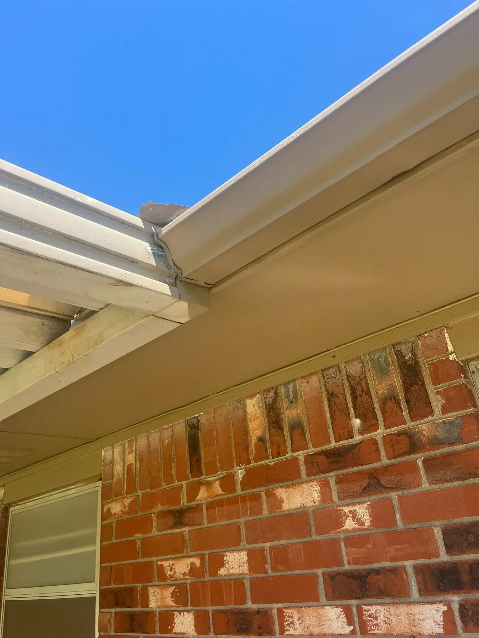 Tan gutters and fascia on brick building under a clear blue sky.