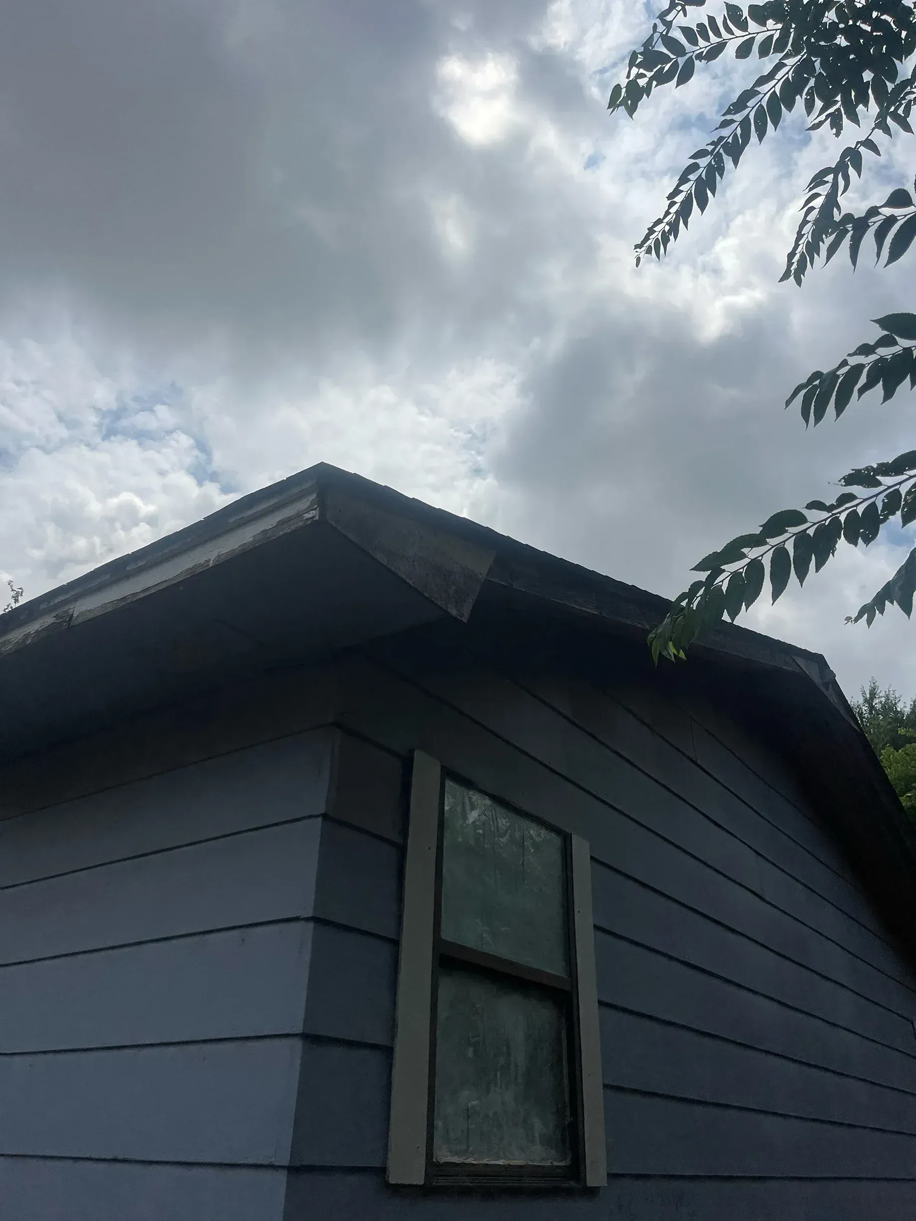 Blue house corner with a window and cloudy sky.