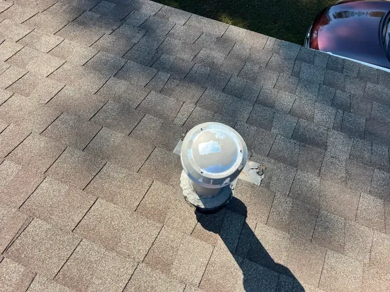Roof with brown shingles, vent pipe, and part of a red car in the upper right.