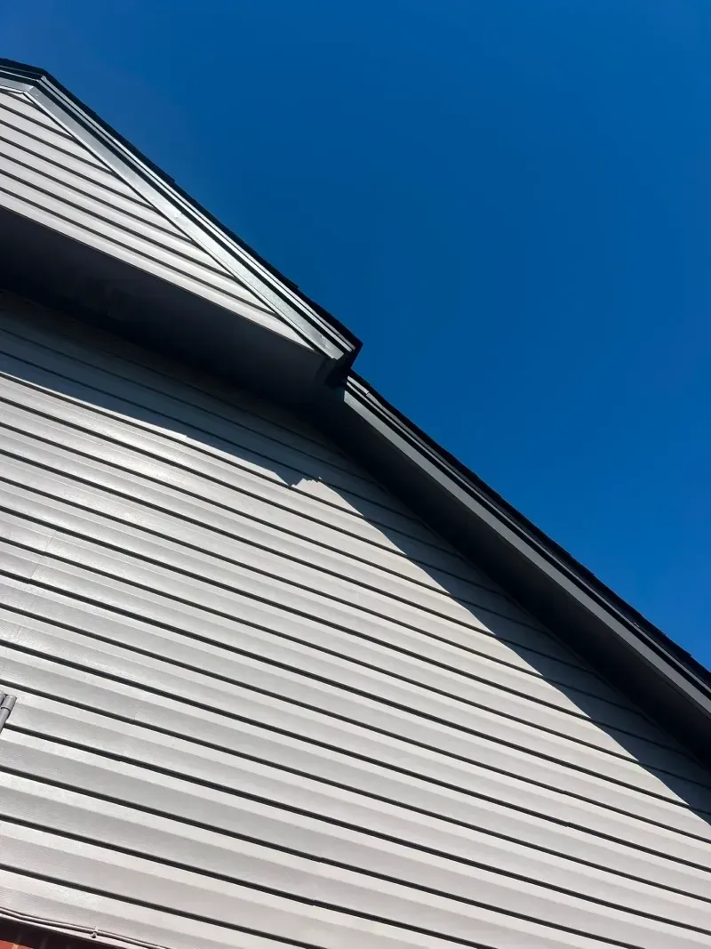 Gray siding on a building with black trim against a bright blue sky.