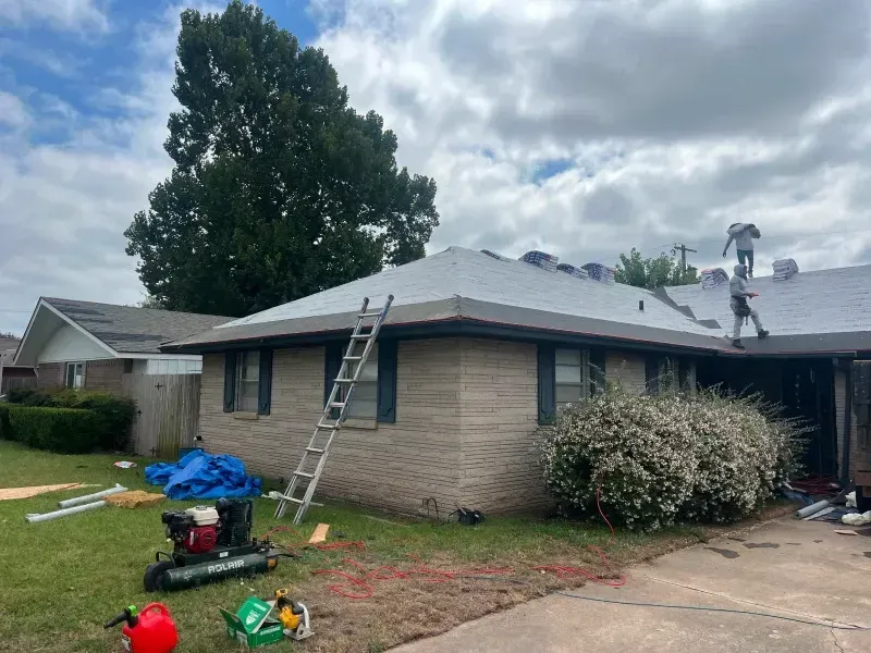 Roofers working on a residential house with a ladder and equipment on the lawn. Cloudy sky.