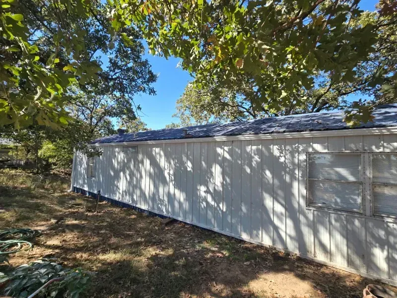 White building exterior with a shaded roof. Sunlight casts shadows on the wall. Overhanging tree branches.