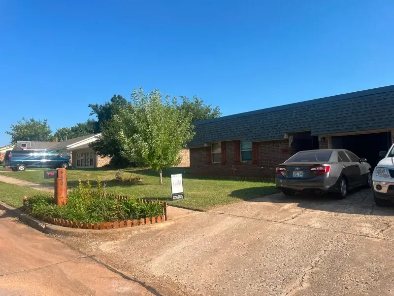 Houses with cars parked in driveways and a for-sale sign on a sunny day.