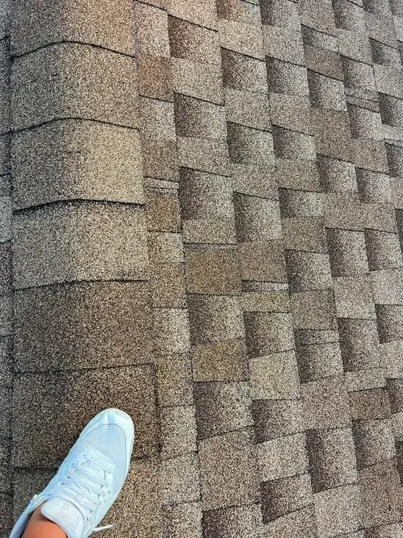 Foot with white shoe on textured asphalt shingle roof.