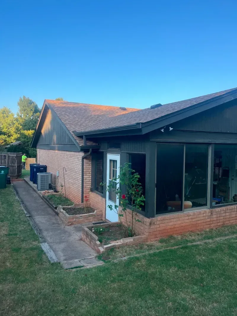Brick house with dark trim and tiled roof. Glass-walled sunroom and small garden beds.