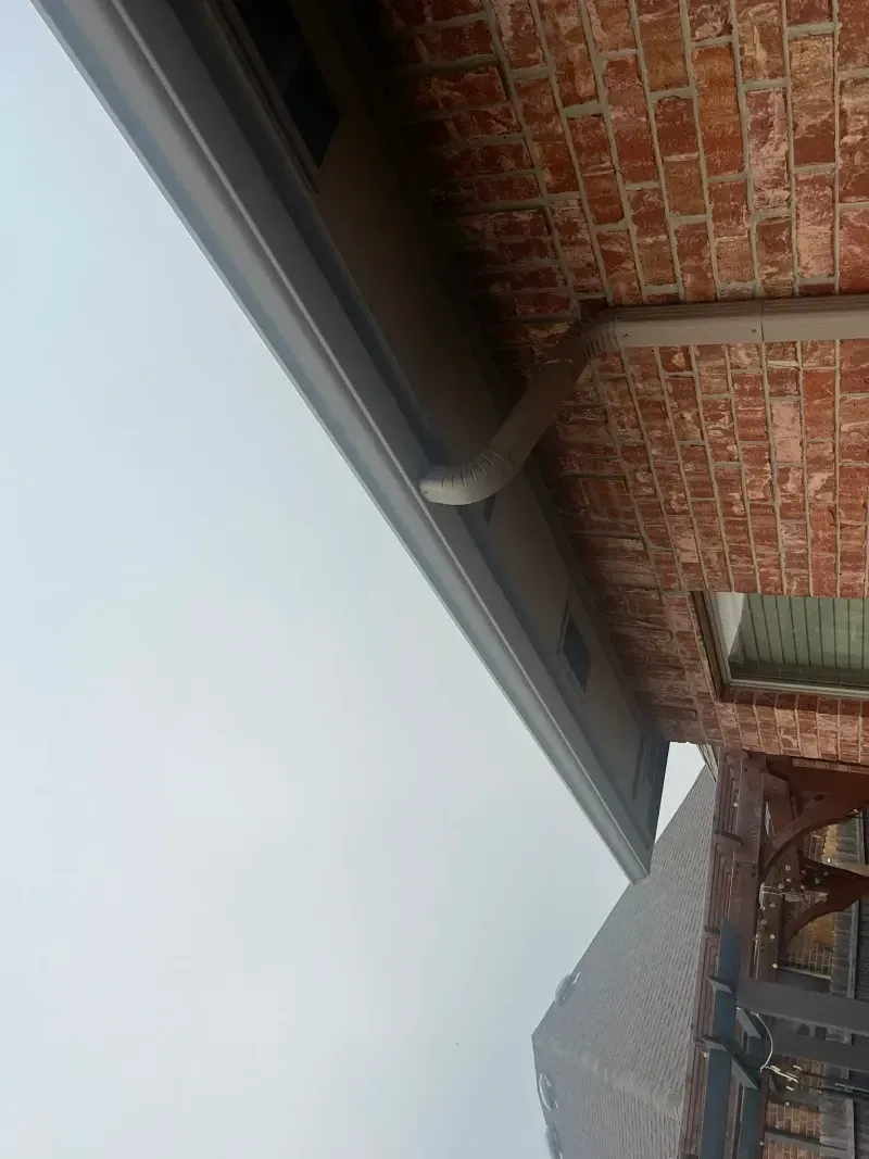 Brick building exterior with gutter and downspout under an overcast sky.