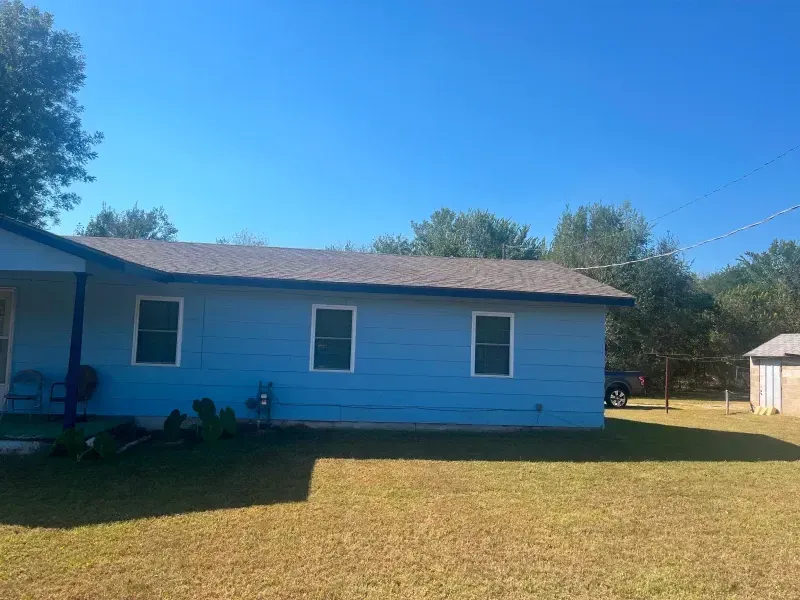 Blue house with a dark roof and three windows. Green lawn under a blue sky.