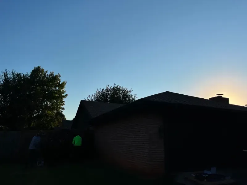 Silhouette of a brick house with a dark roof and a tree against a blue sky at dusk.
