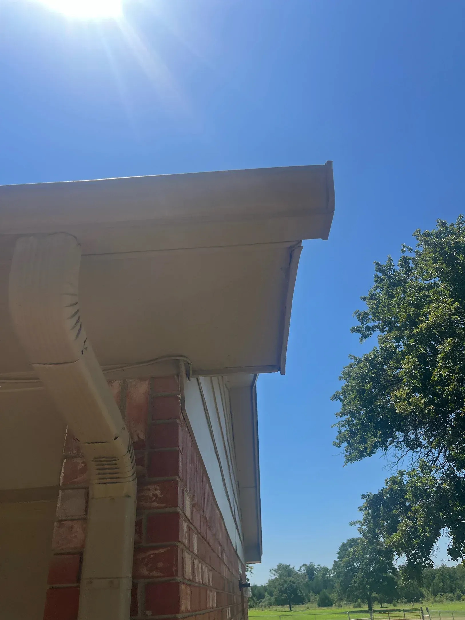 A portion of a building exterior with a light-colored roof, gutter, and brick wall under a blue sky.