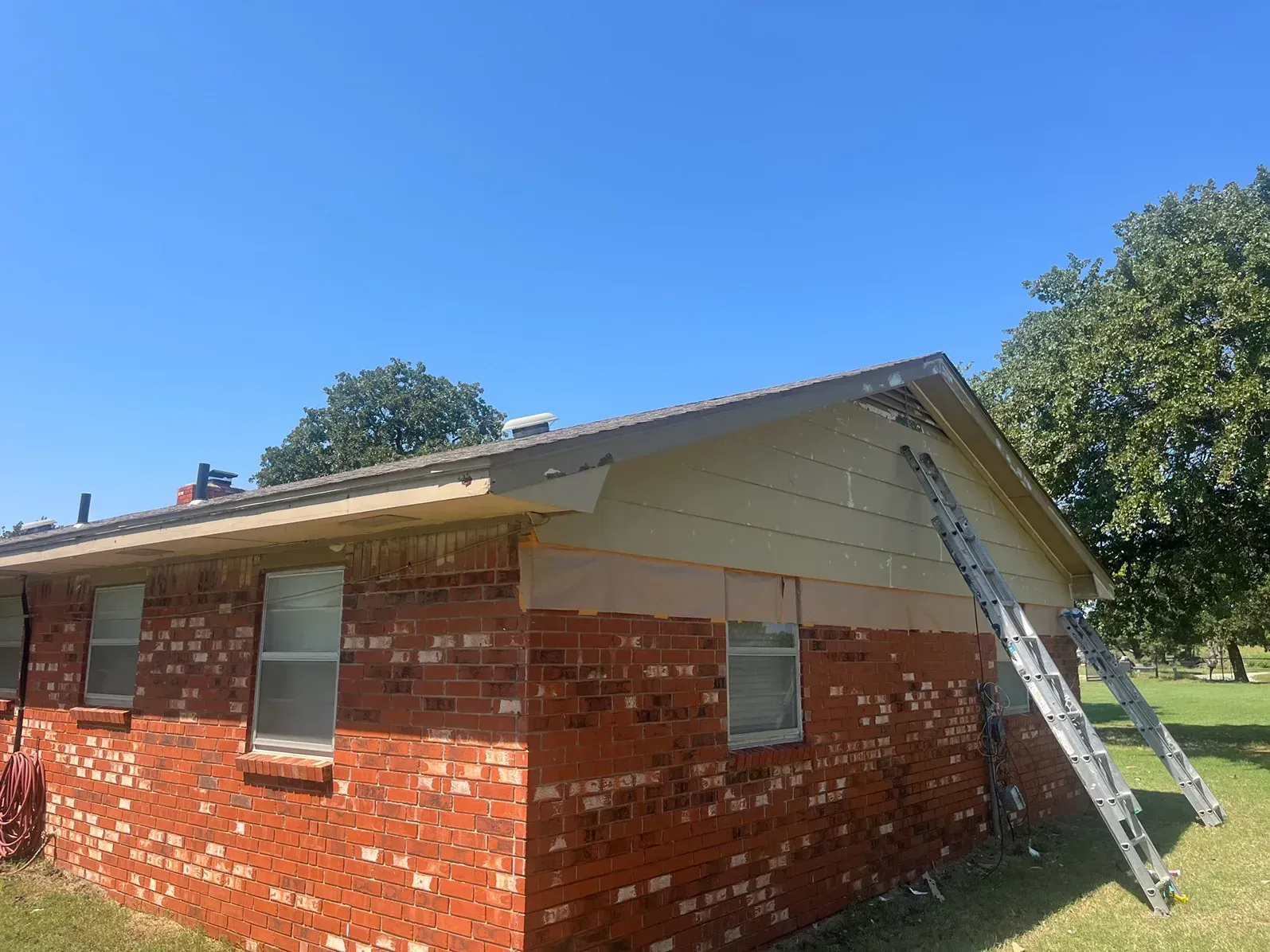 Brick house with a ladder propped against the roof under a bright blue sky.