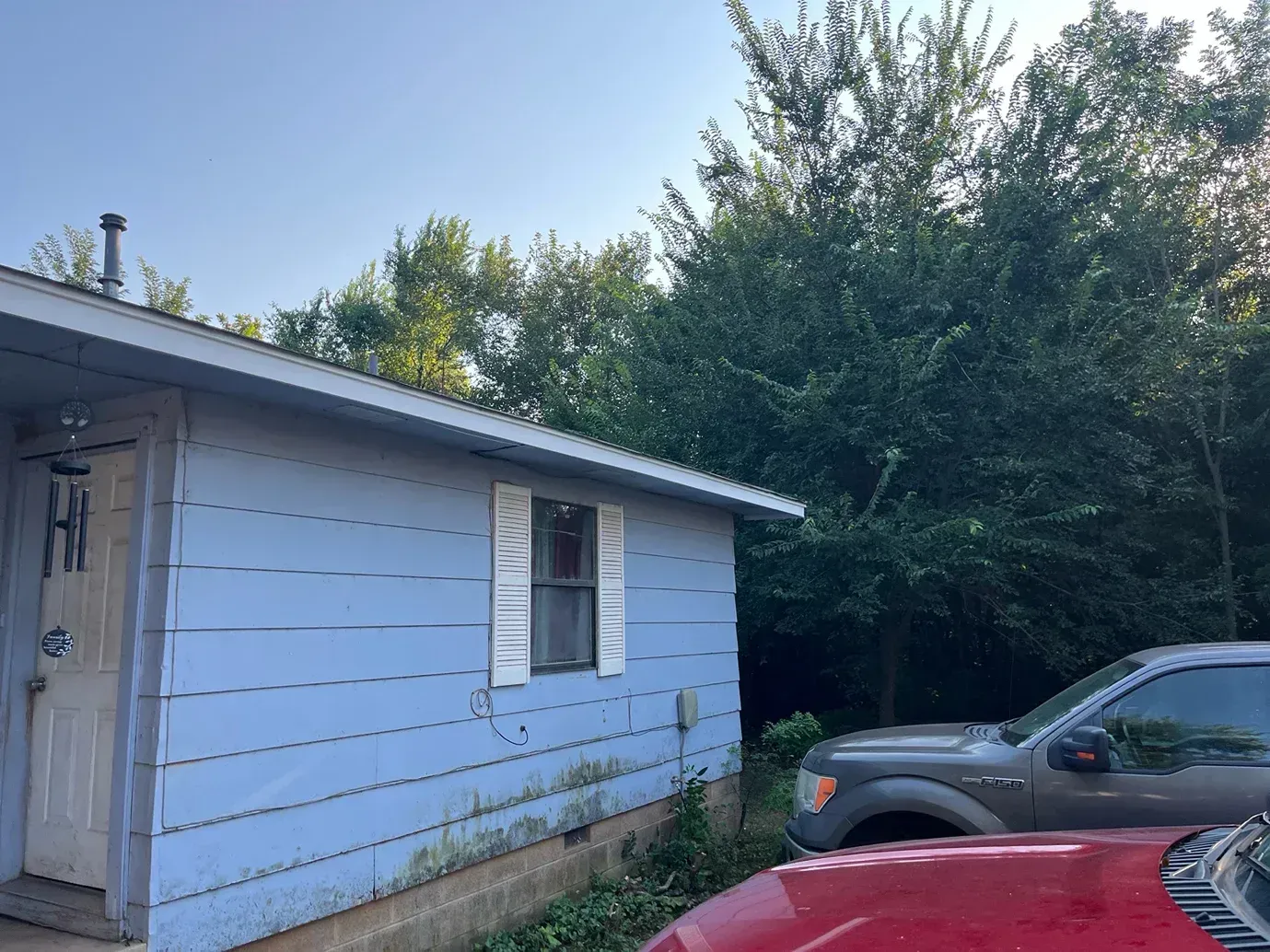 Blue building with a white window and a gray truck in front of a tree.