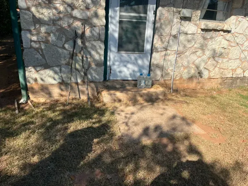 Stone-faced building with white door, concrete steps. Grass and shadows in front.