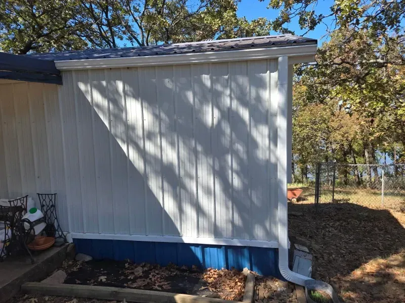 White-sided building with gutter, blue foundation, and surrounding trees in a natural setting.