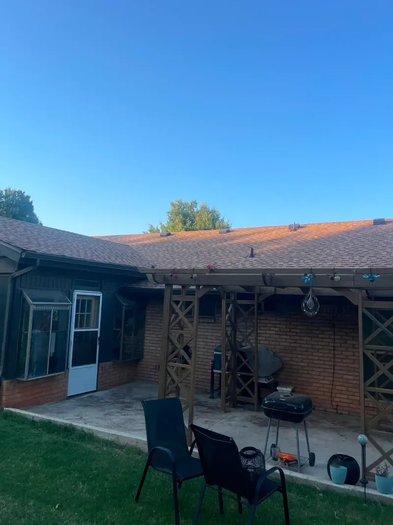 Patio with chairs, grill, and brick wall under a terracotta-tiled roof against a blue sky.