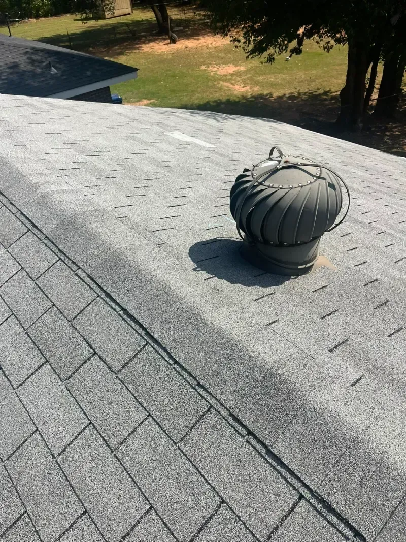Gray asphalt shingle roof with a spinning turbine vent; sunny outdoor setting.