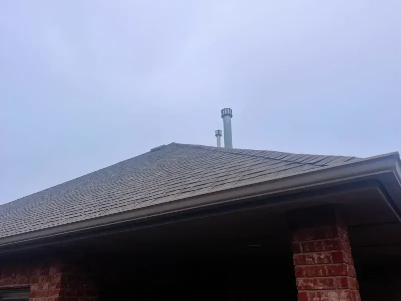 Brown roof with two silver vents against a cloudy sky. A brick wall forms the building's base.