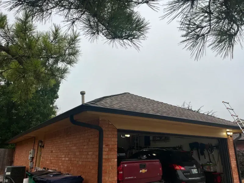 Brick garage with a brown roof and black gutters. Two cars inside, under an overcast sky.