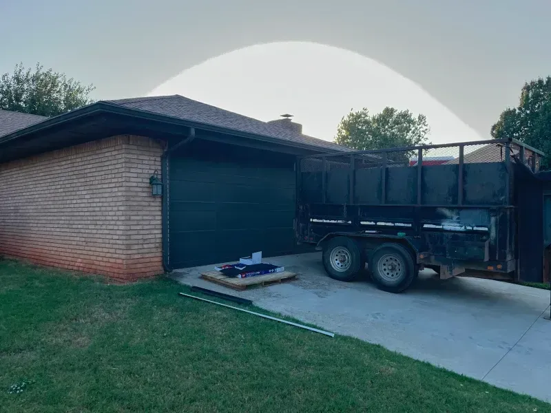 Brick house with a black garage door. A trailer is parked in the driveway. Green lawn.