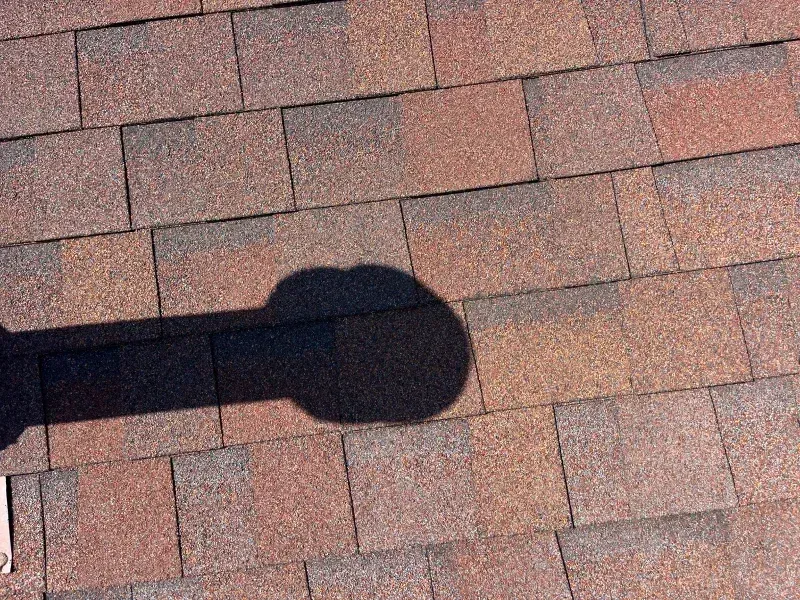 Brown asphalt shingle roof with a shadow of a round object.