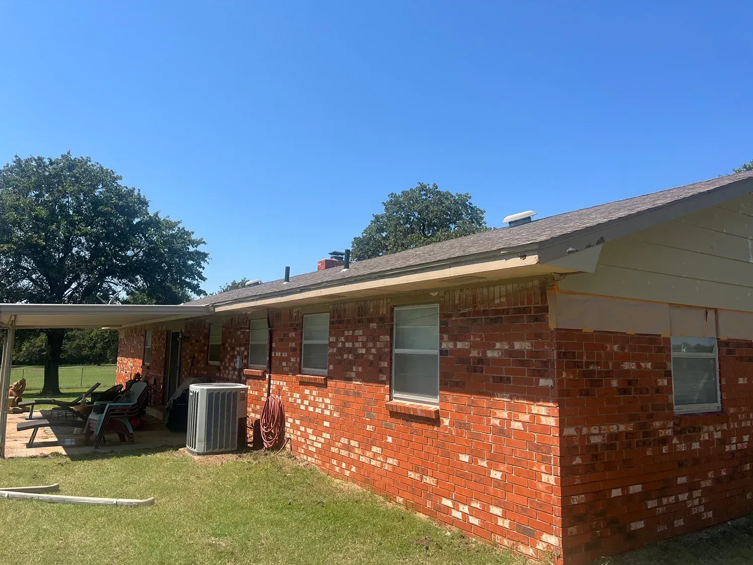 Red brick house with a covered patio and air conditioning unit on a sunny day.