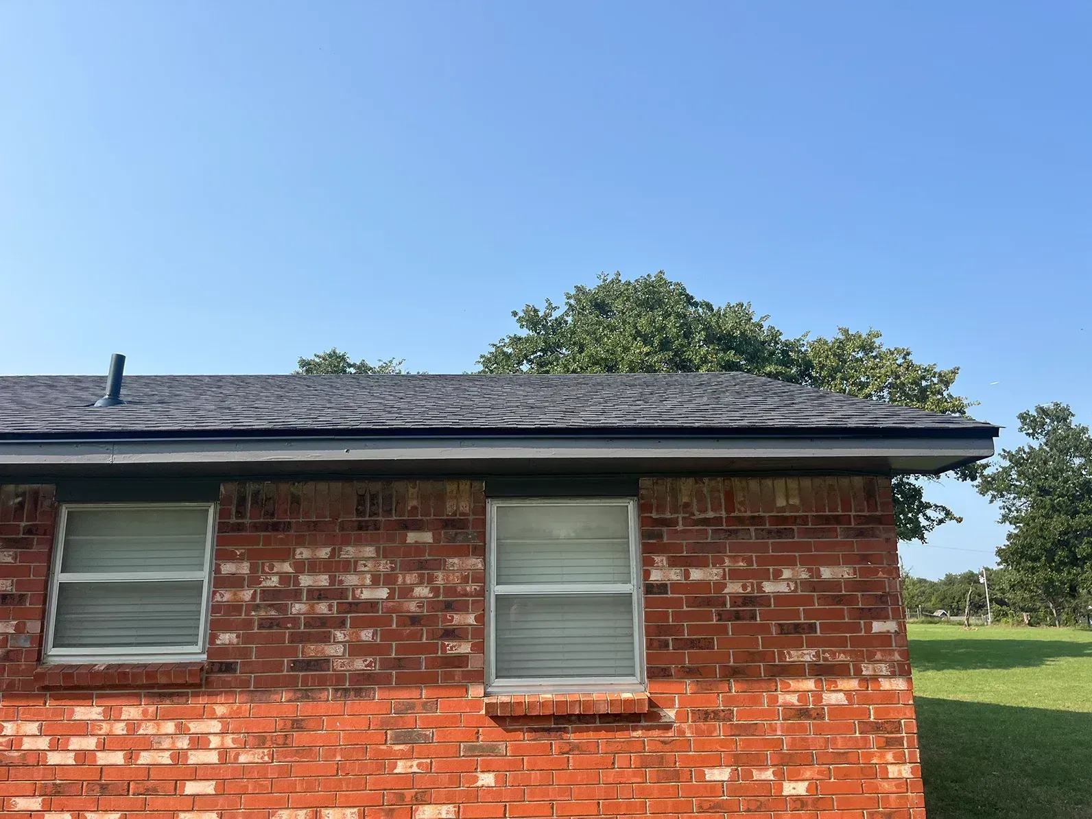 Brick building with dark roof, windows, and clear blue sky.