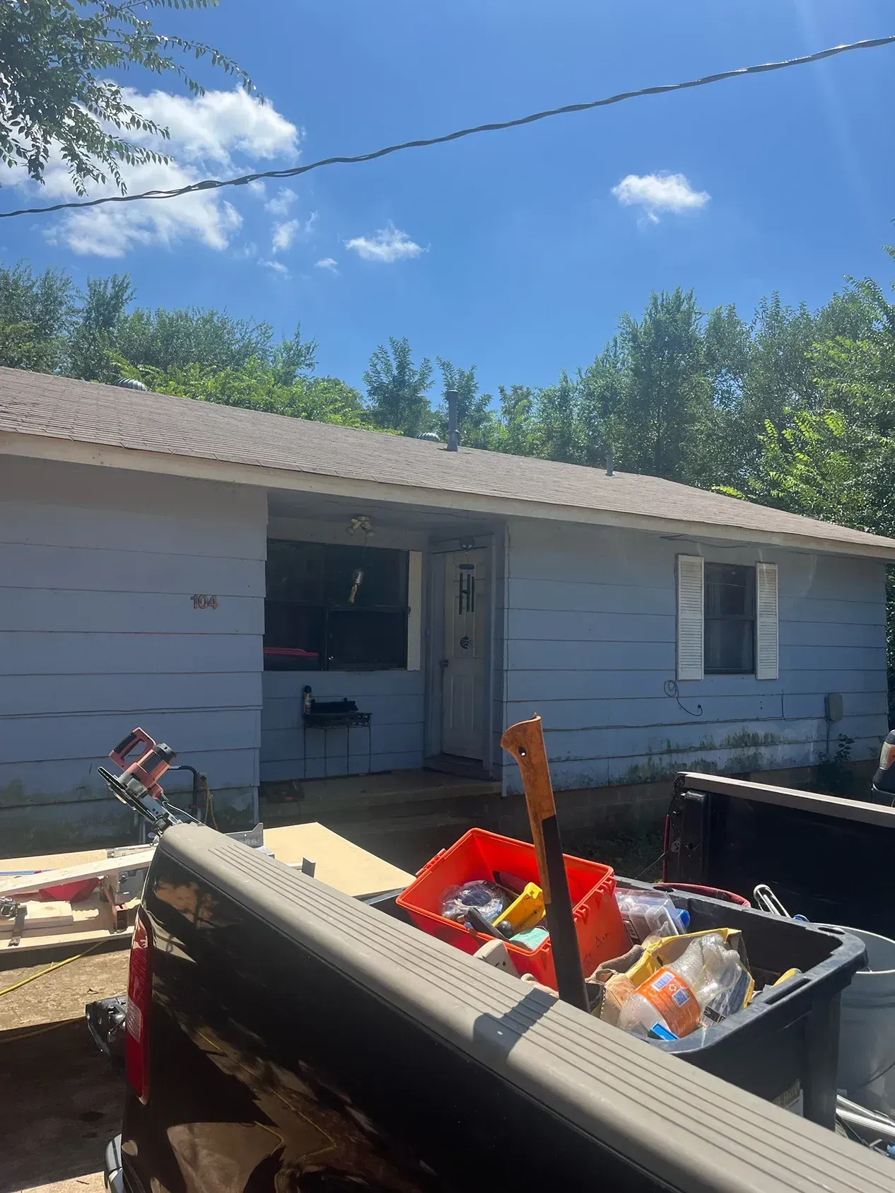 Blue house with brown roof; tools in truck bed in foreground; sunny sky.