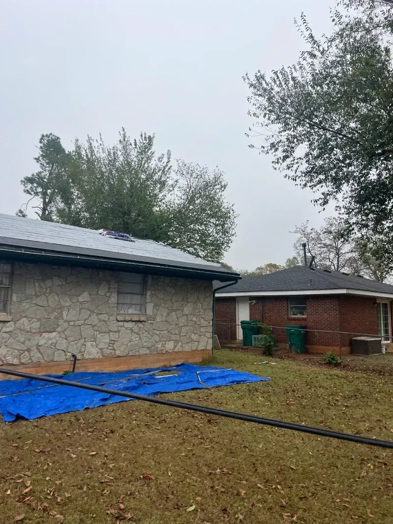 Two houses, one stone, one brick, on a cloudy day. Blue tarp on the ground.