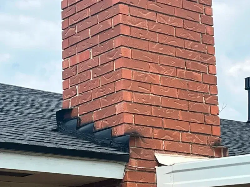 Brick chimney on a roof with black flashing.