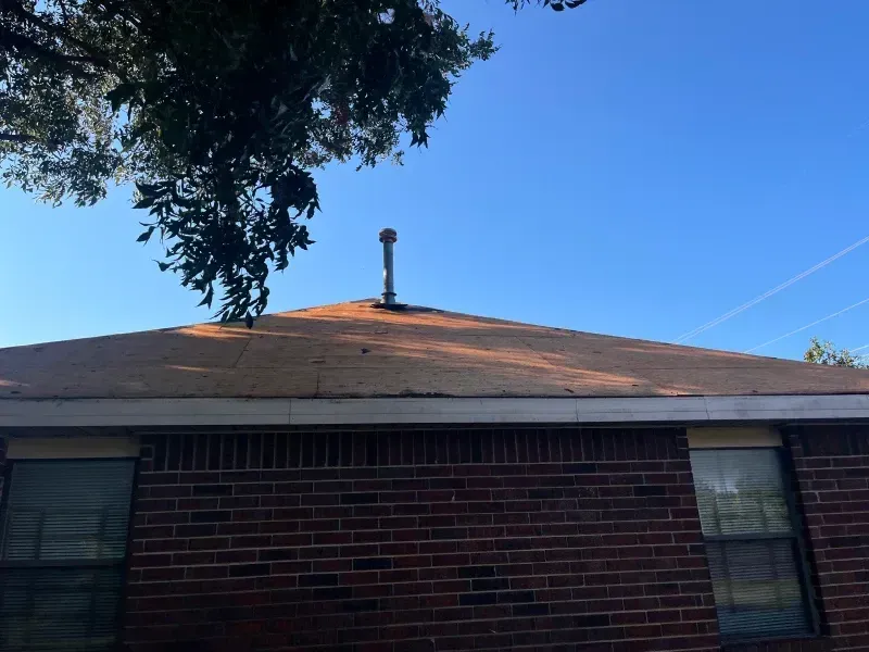 Red brick house with brown roof and metal chimney against a blue sky.