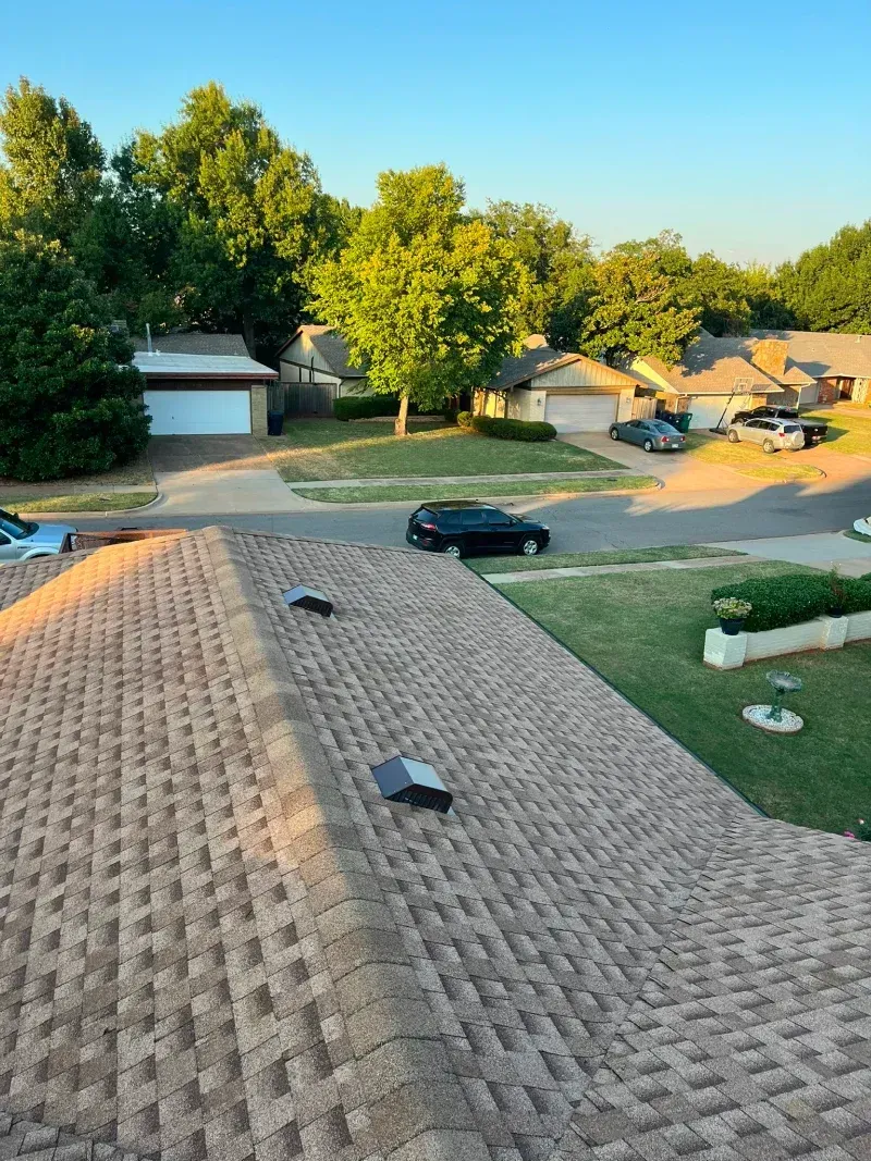 Rooftop view of a residential neighborhood with green trees, driveways, and cars.