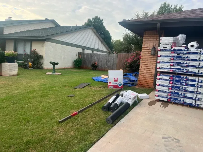 Materials stacked on a driveway next to a house with a green roof, indicating roof repair.