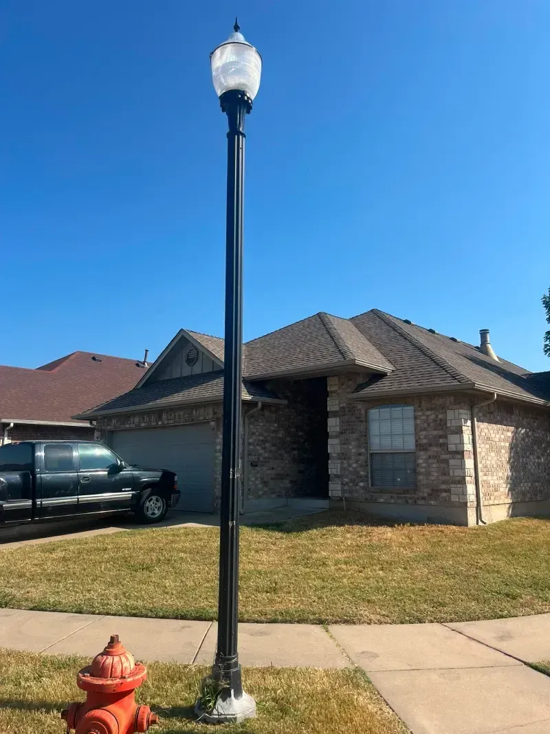 Black lamppost in front yard with red fire hydrant and house with blue sky background.