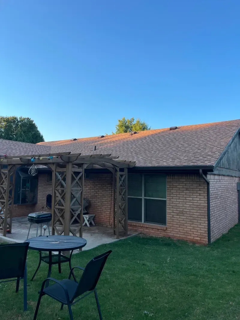 A brick house with a pergola, a patio set, and a grill, set against a clear blue sky.