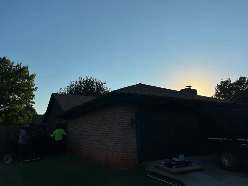 House exterior with workers; dusk sky, brick, dark roof, trees, and tools visible.