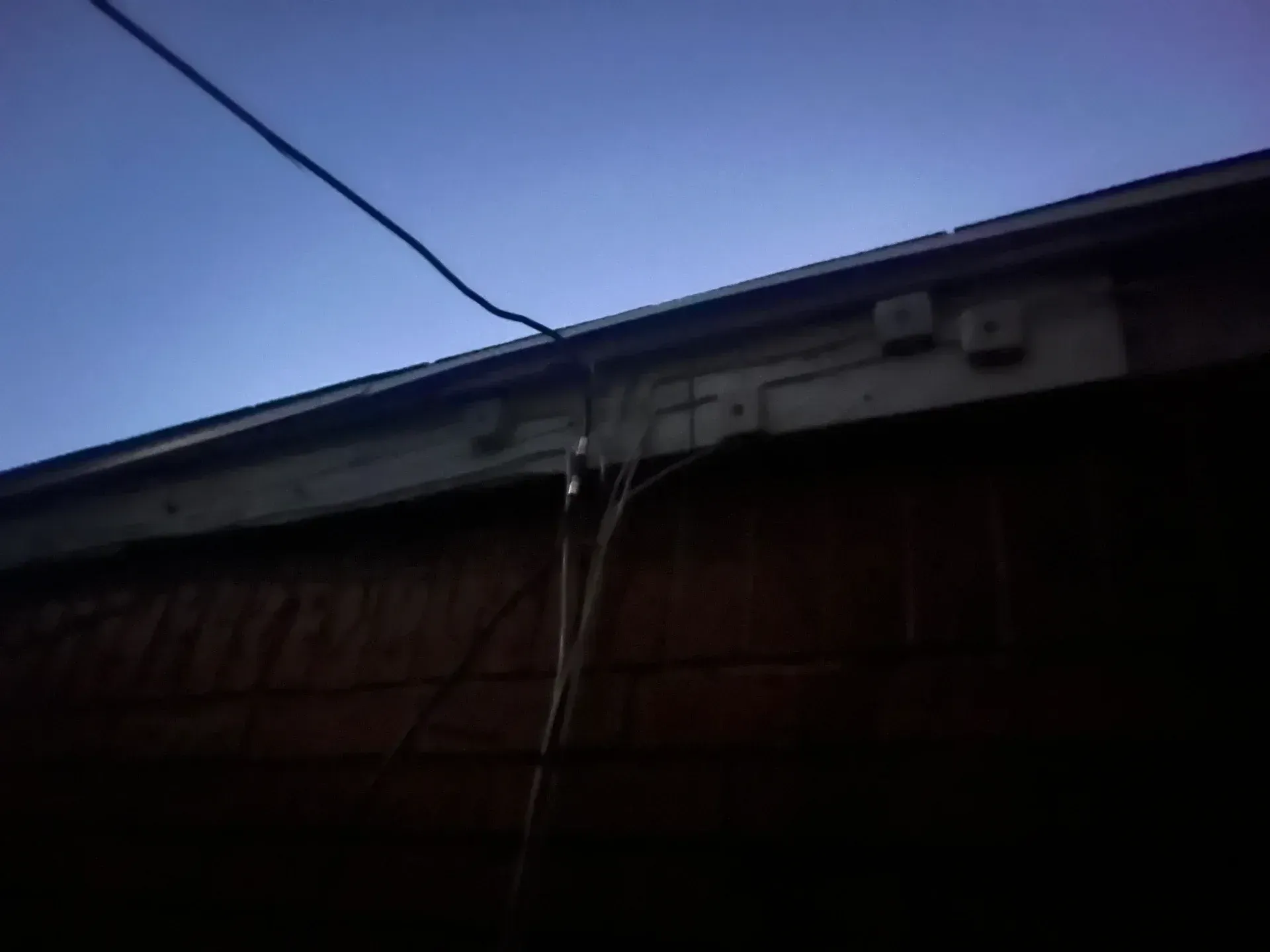 Exterior view: wires and electrical boxes on a building's trim, against a dusky blue sky.