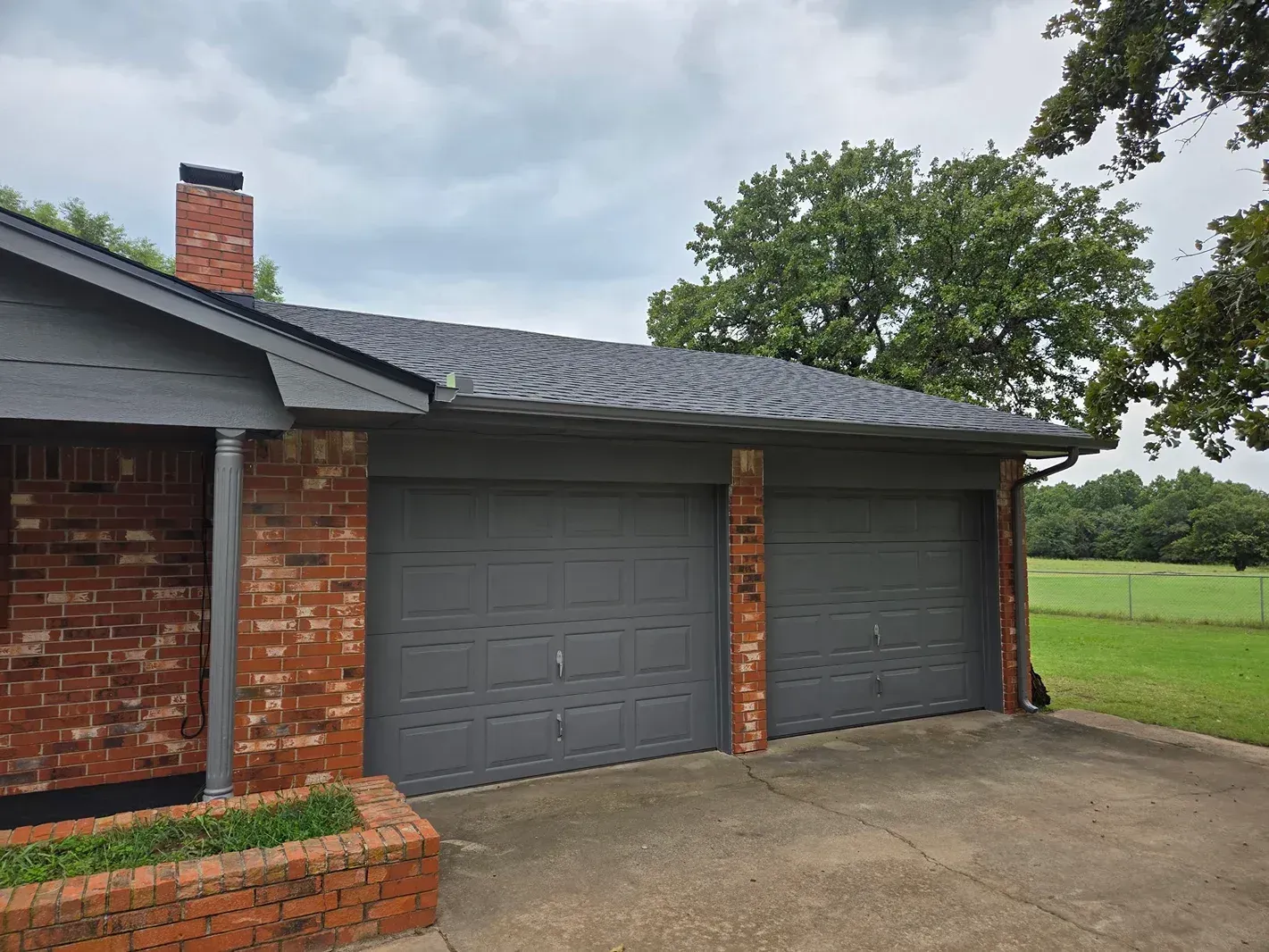 Brick house with gray garage doors and roof. Overcast day.