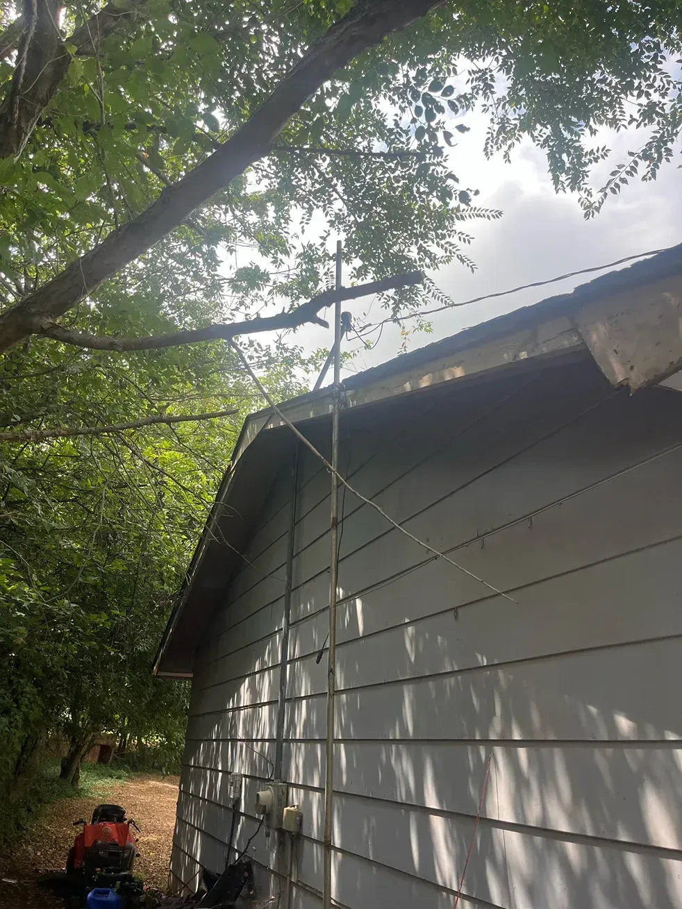 Side view of a light gray building with wires and a tree branch overhead on a cloudy day.