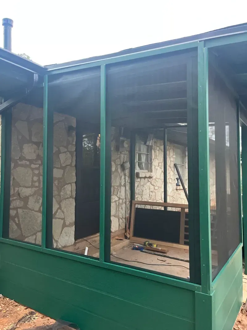 Green screened-in porch with stone walls, partially furnished, viewed from outside.