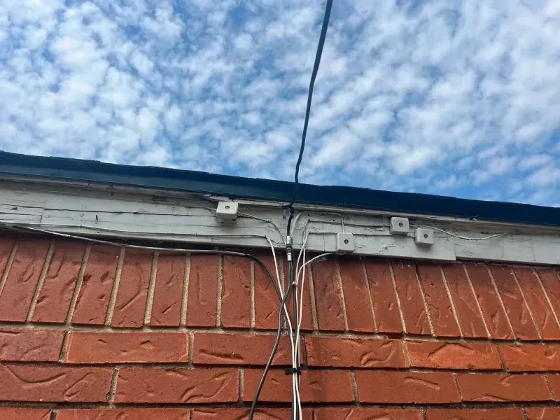 Wires and brackets secured to a brick building under a cloudy sky.