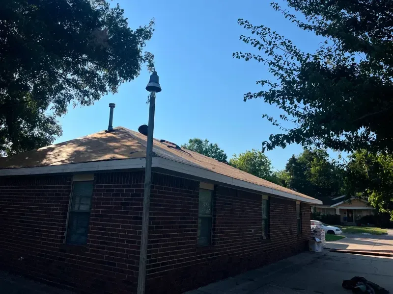 Brick building with roof under construction; a light pole and trees in the blue sky.