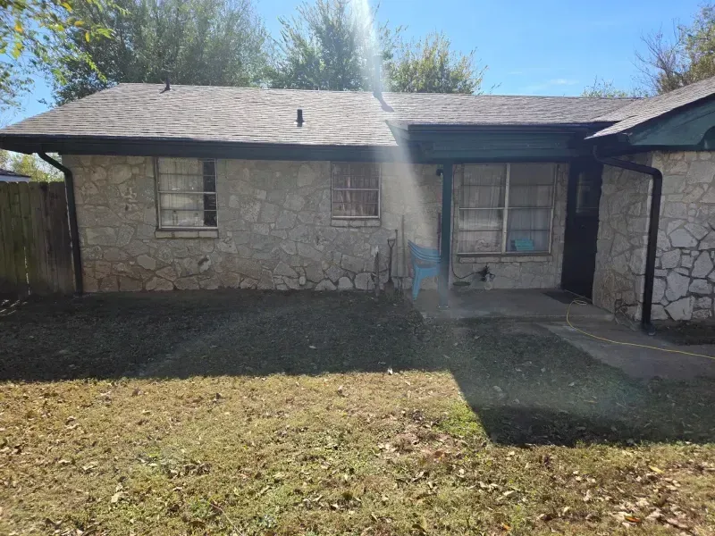 Stone-faced house with brown roof and lawn, under a bright sun.